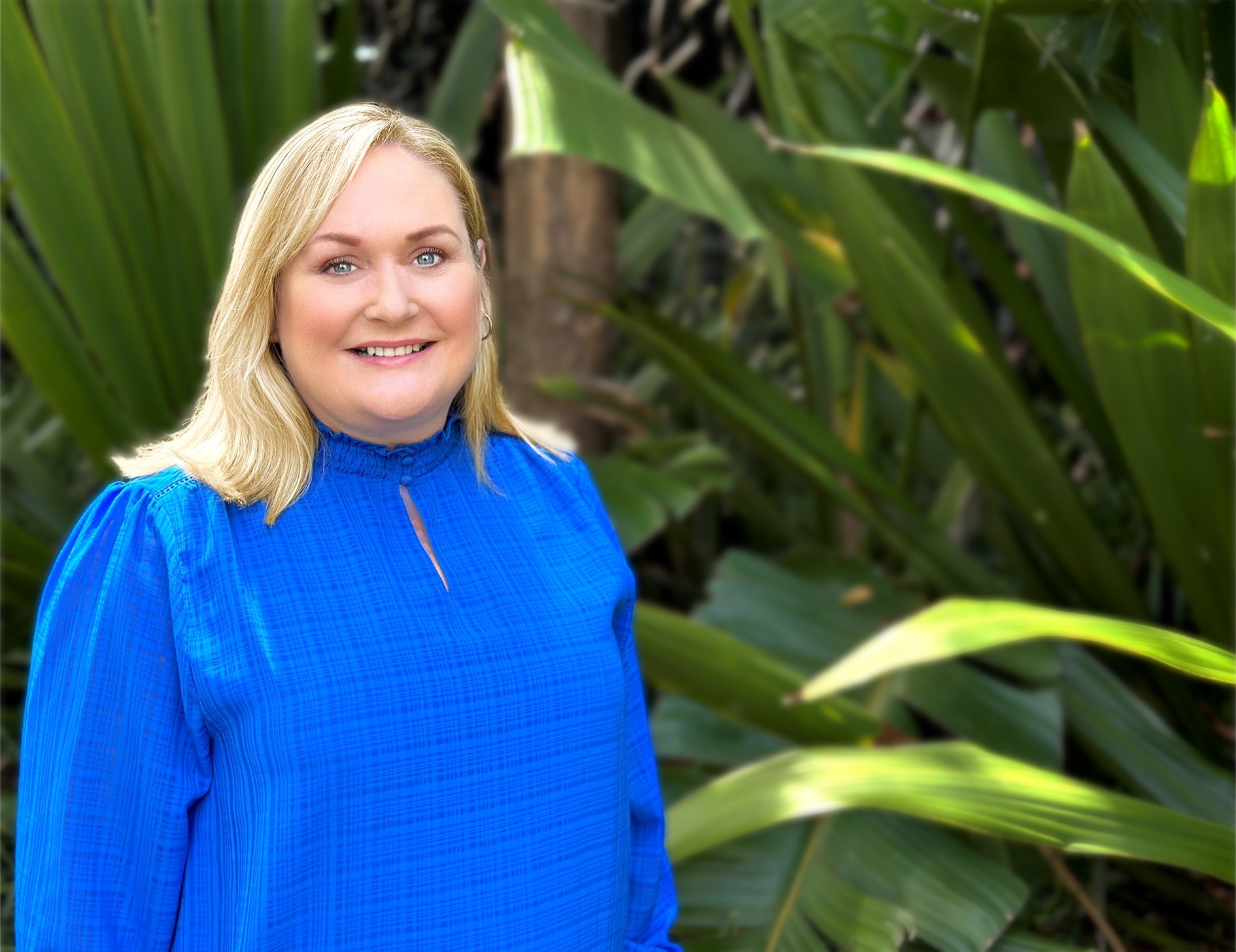 Blonde woman standing in front of tree in blue jumper