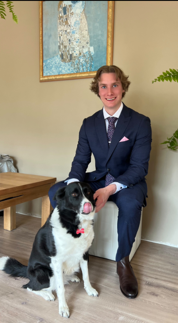 Bachelor of Business and Undergraduate Certificate in Climate Accounting student Myles Hall wears a dark blue suit, seated, patting his dog.