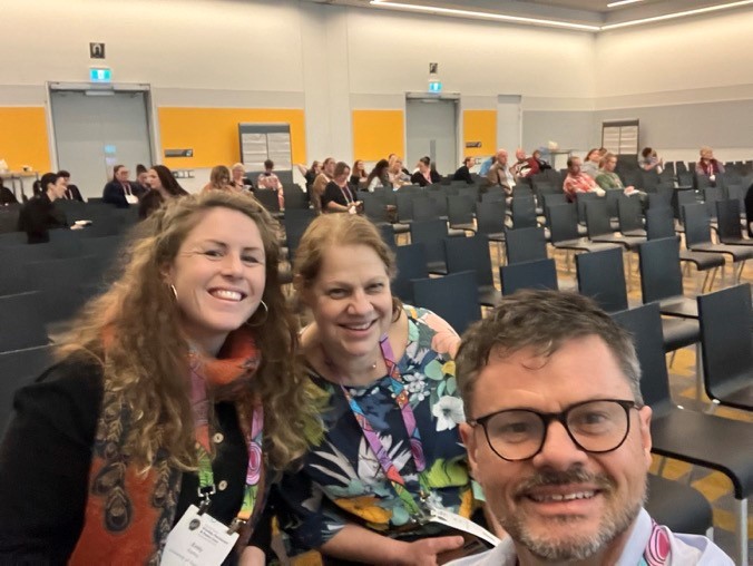 Dr Emily Rudling, Professor Kitty te Riele and Professor Daryl Higgins at the National Care Conference. They are sitting in a lecture room towards the front and smiling at the camera.