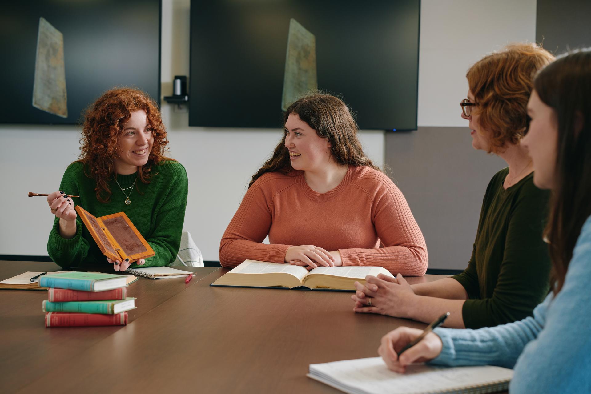 Three female students and a female lecturer sitting around a table with books open