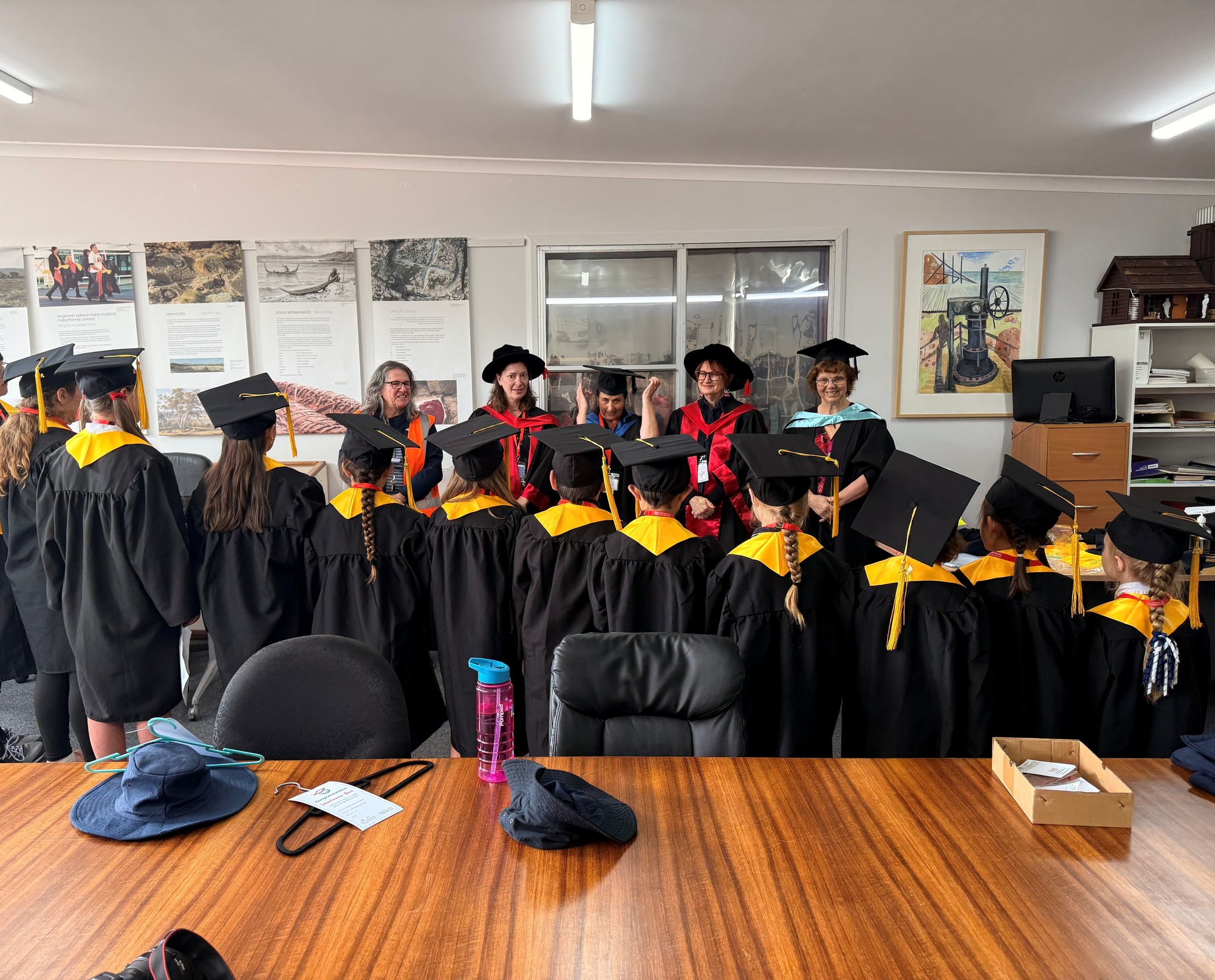 Children's University students line up in their gowns and caps from smallest to largest, and stand in front of five adults also wearing caps and gowns.