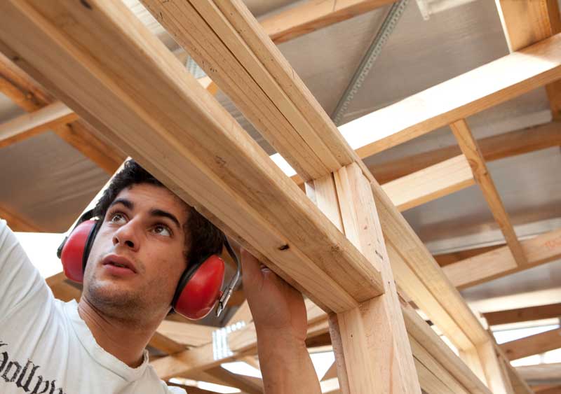 Student working on timber frame structure wearing safety ear protectors.