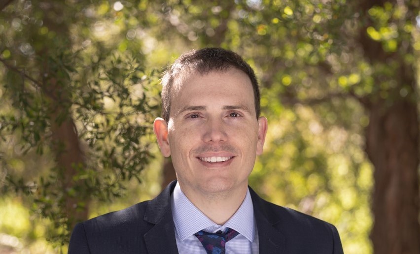 Saul is smiling, wearing a blue suit and tie.