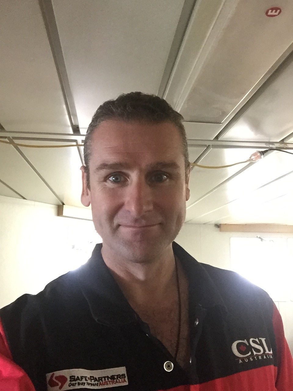 A smiling caucasian man with short brown hair wearing a black and red polo shirt.